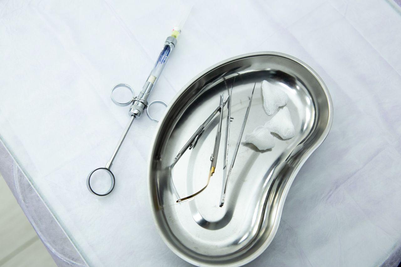 A set of sterile medical tools and syringe displayed in a kidney tray for dental or surgical use.